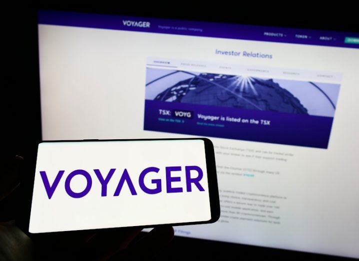 A smartphone screen showing the Voyager logo with a computer screen in the background.