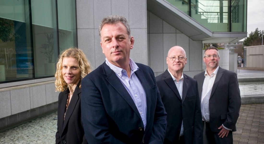 A woman and three men stand next to each other wearing business formals. They are standing in front of the Sage HQ building.