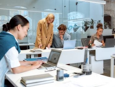 A group of people in an office, some are sitting at computers while others are standing around.