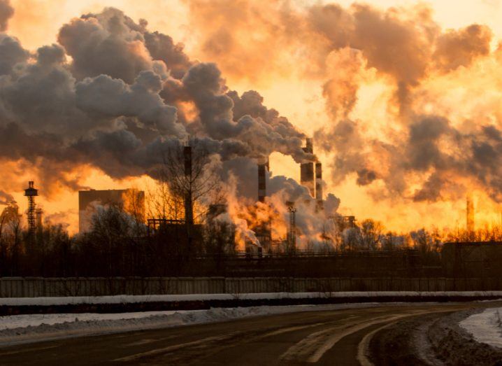 Smoke coming out of multiple factory chimneys with an orange sky in the background.