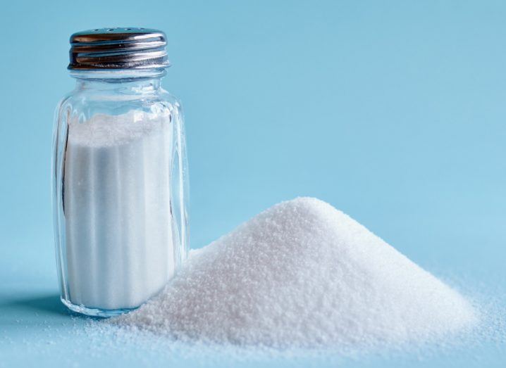 Salt shaker and a pile of salt against a blue backdrop.