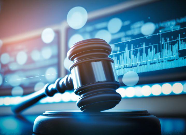 Illustration of a court gavel on a table, with blue screens and graphs in the background.