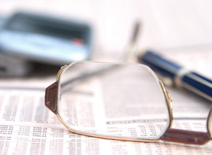 A pair of glasses on top of a piece of paper, with a pen visible in the background.