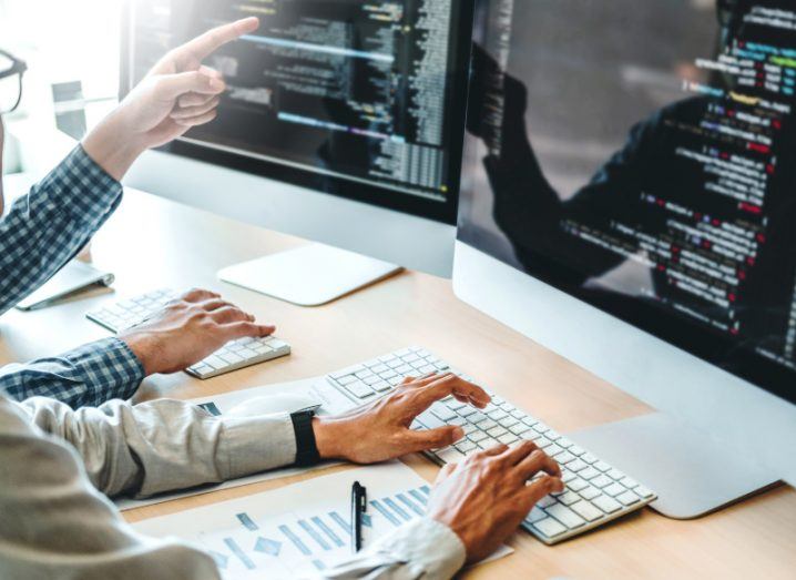 Two people are sitting at Apple desktop computers and working on coding software. It shows what designing the Fineos software might be like.