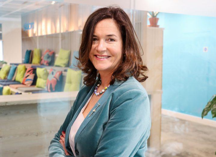 A woman stands smiling with her arms folded, standing with her side facing the camera, with an office setting behind her. She is Jane Dawson-Howe, country leader of Slalom Ireland.