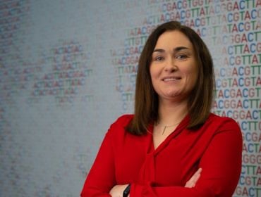 A woman wearing a red blouse smiles at the camera with her arms folded. She is Karen Breen, a risk and business performance director at Amgen.