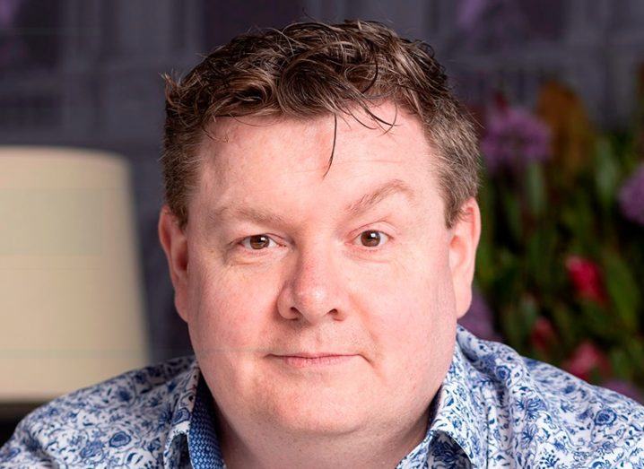 A man smiles at the camera wearing a patterned shirt. He is Kieron Smith, CTO at SnapDragon Monitoring.
