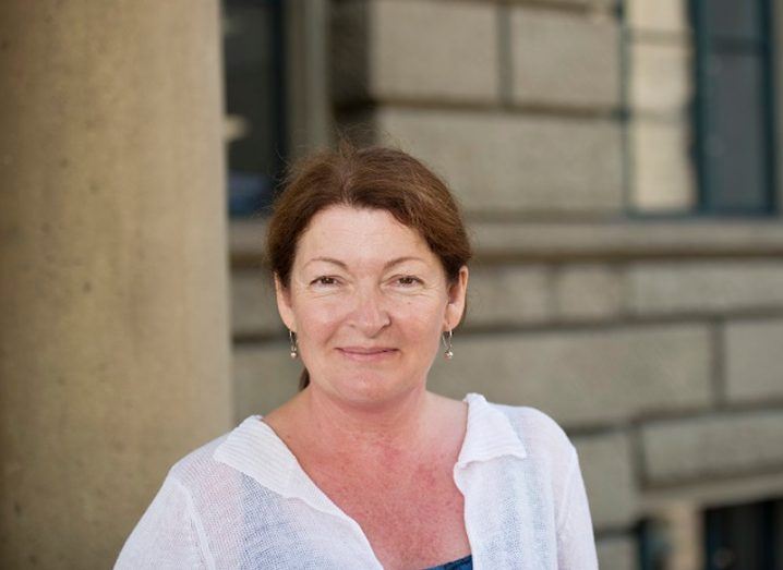 A woman smiles at the camera in front of a white building. She is Dr Catherine Richards Golini.
