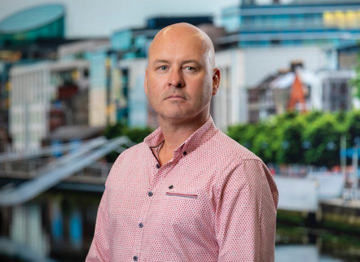 A man looks at the camera wearing a pink shirt, with a blurred cityscape behind him. He is Tom Gorman, director of operations at Digital Realty.