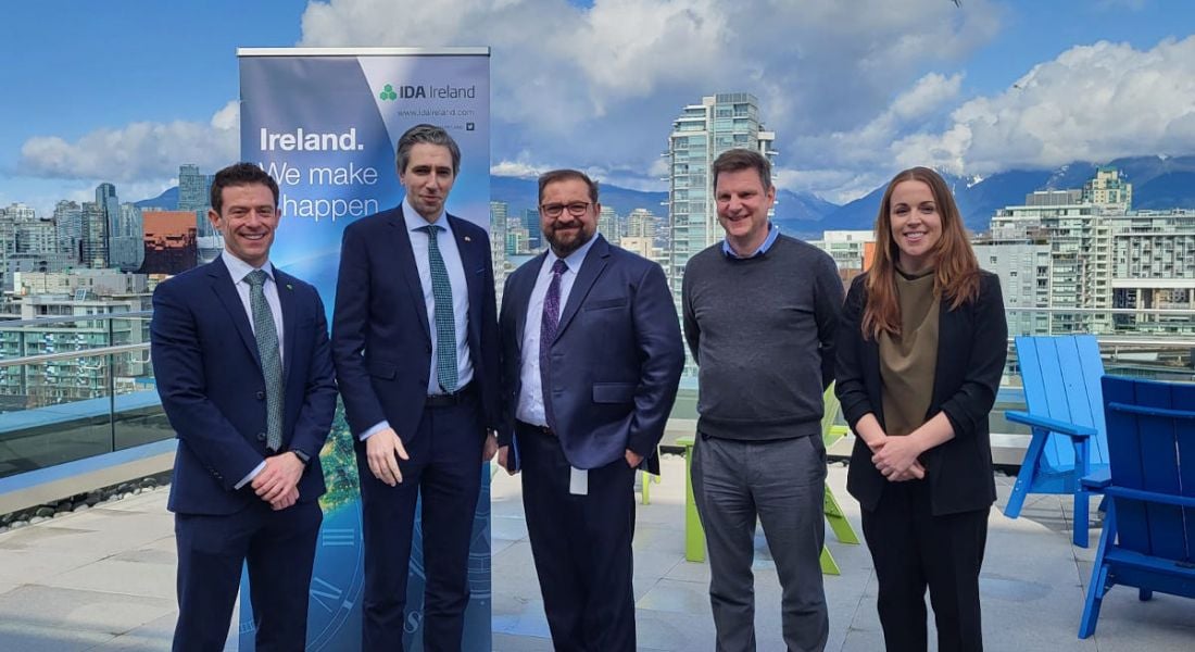 Four men and one woman stand outdoors in front of an IDA Ireland banner smiling at the camera.